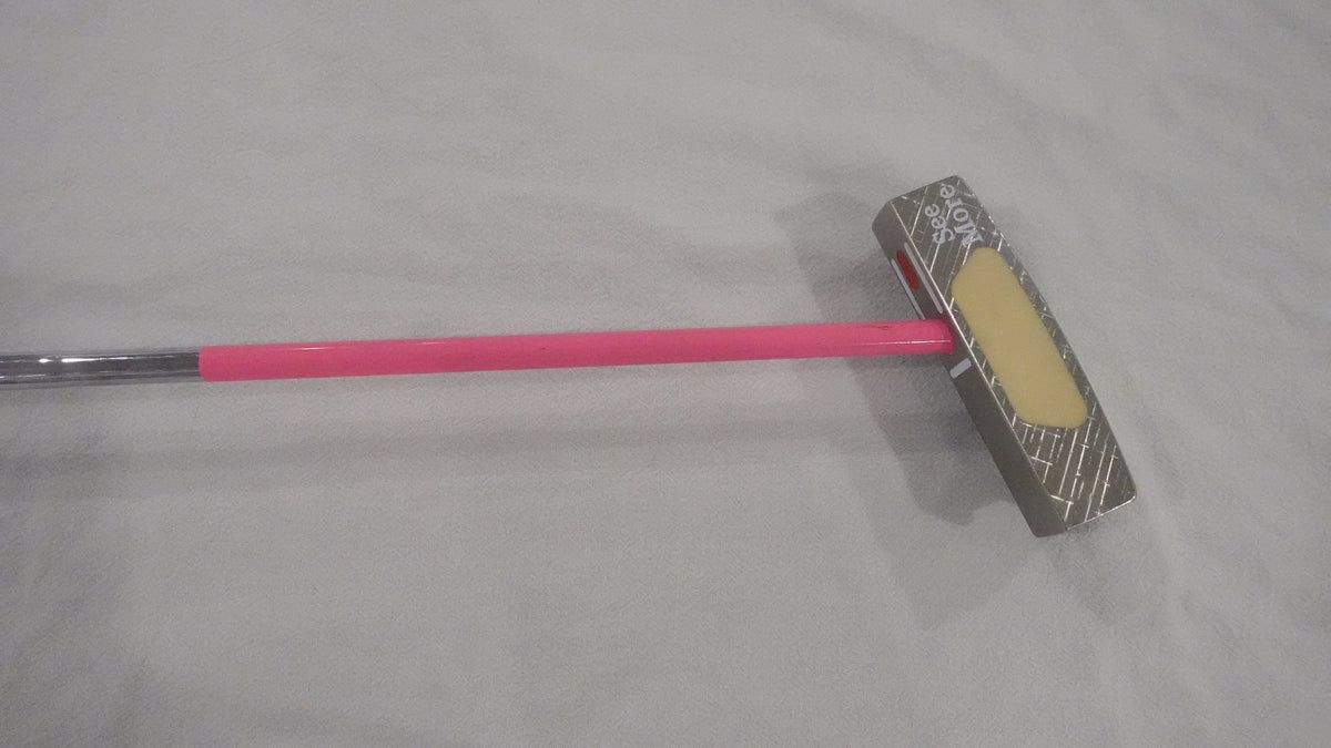 A pink and silver golf putter head with a yellow face, resting on a light gray fabric background.